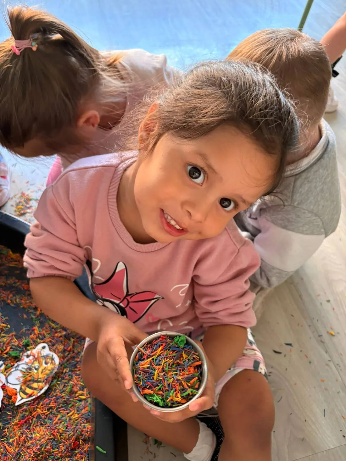 Niña sonriendo con un cuenco de materiales de colores